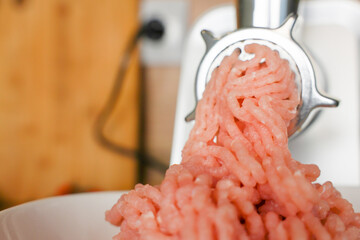 Close-up view: pink minced turkey comes out of a metal meat grinder and sinks into a white plate on...