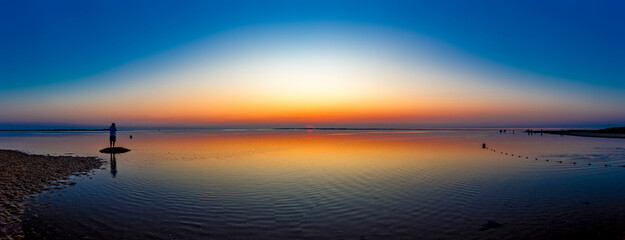 Ein nicht erkennbarer Mann beobachtet den Nachglanz eines Sonnenuntergangs am Strand von Utersum bei ruhiger See und wolkenlosem Himmel