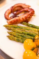 Deliciously succulent grilled octopus beautifully served with fresh, tender asparagus and vibrant cherry tomatoes
