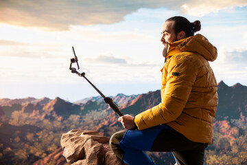 Traveler filming his hiking experience in the wilderness documenting his adventure on social media using his smartphone. Recording the beautiful scenic mountain view behind him for content.