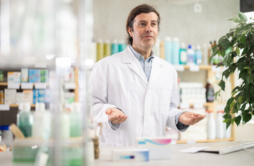 Man pharmacy employee works at computer, reads handbook on pharmaceutical care and additional...