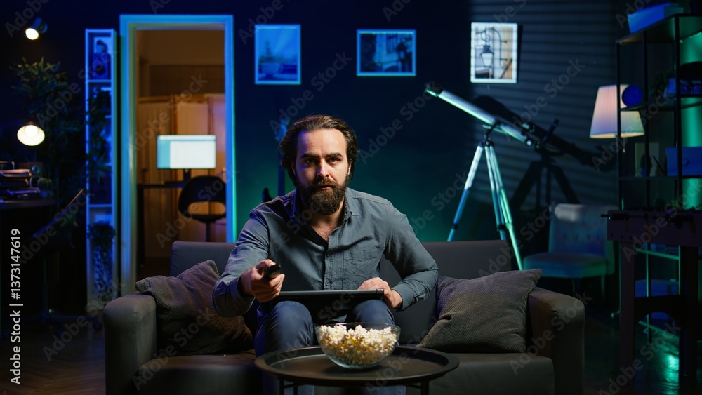 Aufkleber man watching shocking breaking news story on tv while using laptop in neon lit apartment. person tur