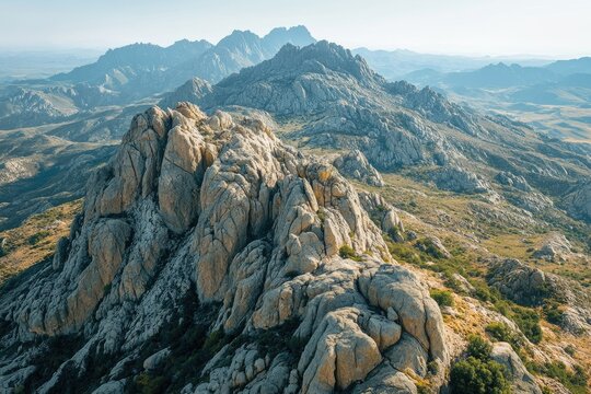 A stunning aerial view of a mountain range with rugged, rocky peaks and sparse vegetation under a clear blue sky.