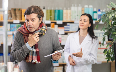 Mature man with a sore throat and cough came to the pharmacy for anti-cold and antipyretic pills. Cold buyer consults with a pharmacist about the choice of pills