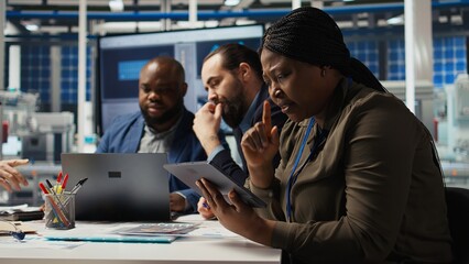 Factory manager works on integrating automation technology in industrial plant, looking at device. African american woman analyzing business model data on tablet, expanding production, camera A