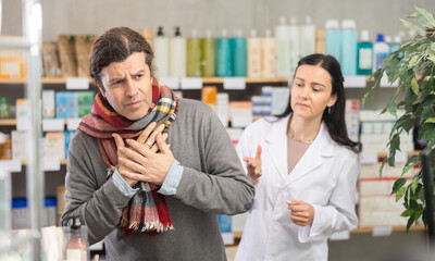 Middle-aged male client needing drugs for cough, female apothecary trying to help him in drugstore
