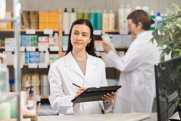 Adult woman pharmacist conducting inventory with tablet in pharmacy