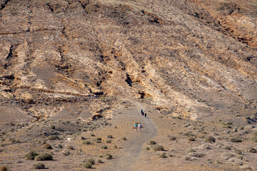 People walking along the foot of the mountain towards Las Grietas, Lanzarote, Canary Islands, Spain.