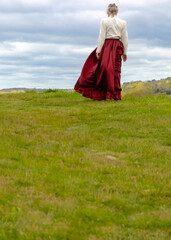 A woman wearing a red skirt and a white blouse stands in a field.