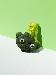 Funny broccoli with googly eyes on a green background. Playful food concept, healthy eating, and vegan lifestyle