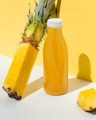 Bottle of fresh pineapple juice with a sliced pineapple on a yellow background. Refreshing tropical...