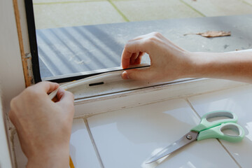 A man insulates a window frame with a rubber profile.