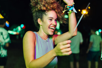 Young woman dancing with sparkler at night festival enjoying music and lights