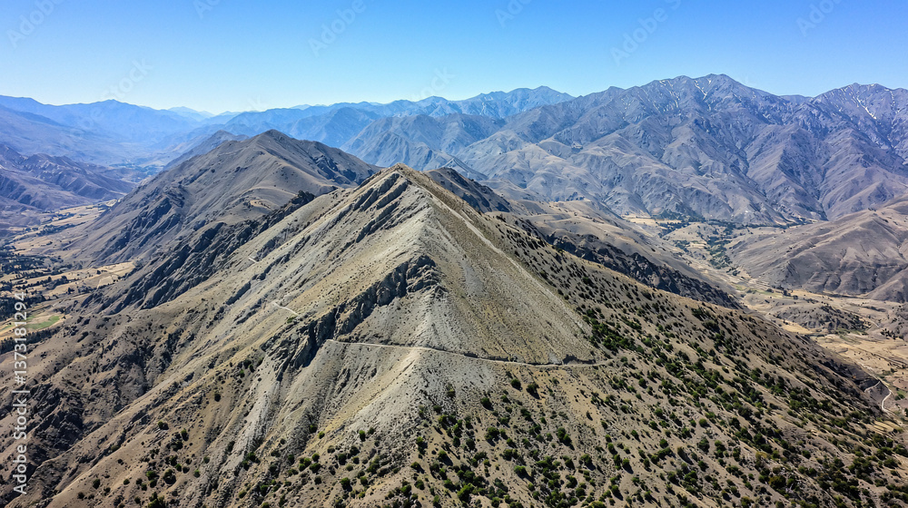 Poster expansive view of a mountain range highlighting the unique features of wind-swept ridges under a rad