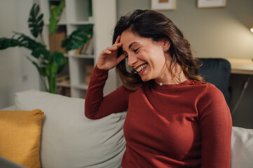 Happy woman laughing while using laptop on sofa at home