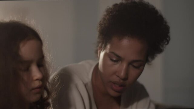 Black mother teaching daughter music from book with syllables