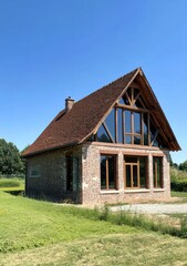 Fototapeta premium Nestled in the picturesque countryside, this stunning house boasts expansive windows inviting warm sunlight inside, embraced by lush green fields and majestic trees in the background.