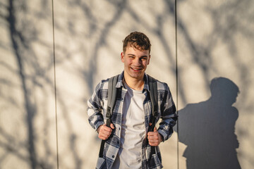 Fototapeta premium young man with wear backpack in front white wall outdoor
