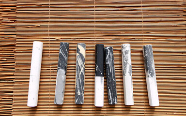 Seven cylindrical sticks in white, black, and gray marbled designs are neatly arranged on a light brown bamboo mat. Simple, neutral, and decorative objects.