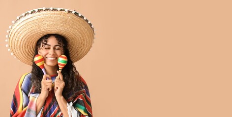 Beautiful young African-American woman in sombrero and poncho playing maracas on beige background...