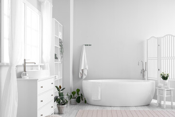 Interior of light bathroom with sink, bathtub, window and houseplants