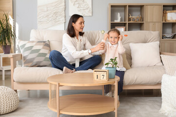 Fototapeta premium Beautiful mother and her cute little daughter with sweet lollipops sitting on sofa at home