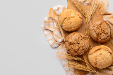 Board with fresh delicious buns and wheat ears on white background