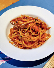 spaghettoni di pasta fresca con gamberi e pomodori rossi, serviti in un piatto bianco al ristorante