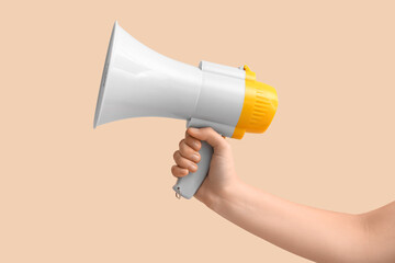 Female hand with megaphone on beige background