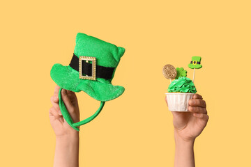 Female hands with tasty cupcake and leprechaun hat for St. Patrick's Day on beige background