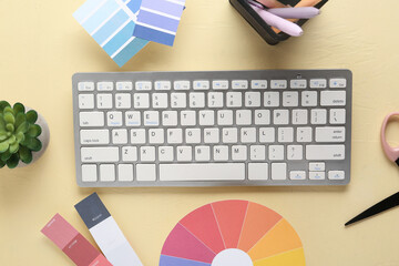Computer keyboard with color samples and stationery on light yellow background