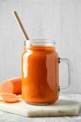 Fresh carrot juice in mason jar and vegetable on gray textured table