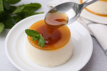 Pouring caramel sauce onto tasty pudding on white table, closeup