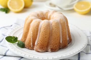 Delicious lemon cake with glaze and mint on white table, closeup