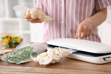 Young woman with vacuum sealer machine for food, parsley and mushrooms in packs on kitchen table