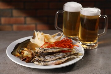 Different dried fish snacks and beer on grey table