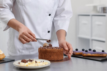 Pastry chef decorating cake with chocolate shavings at table in kitchen, closeup