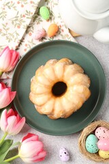 Delicious bundt cake, Easter eggs and tulips on grey table, flat lay