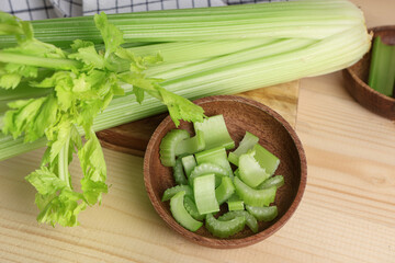 Bowl and board with fresh green celery on wooden background