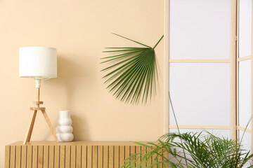 Interior of room with folding screen, commode and houseplants near beige wall