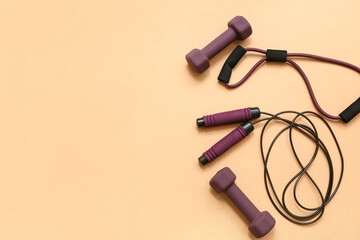 Expander, dumbbells and jumping rope on beige background