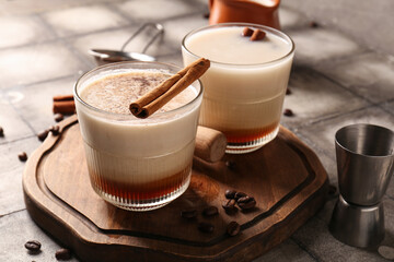 Glasses of White Russian cocktail with cinnamon and coffee beans on grey tile table