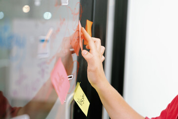 Closeup of professional businesswoman hand put and stick the colorful sticky notes on whiteboard while presenting business plan. Creative business meeting and brainstorming concept. Immaculate.