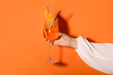 Female hand with glass of Aperol spritz cocktail on orange background