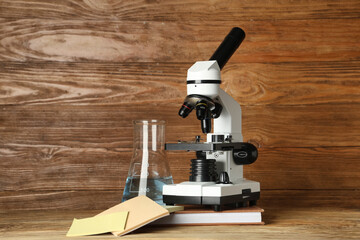 Modern microscope with chemical flask, sticky notes and book on table against wooden background