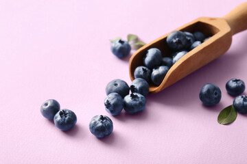 Wooden scoop with fresh ripe blueberry on lilac background, closeup