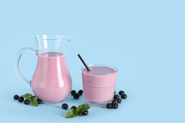 Glass and jug of fresh blueberry smoothie with mint on blue background