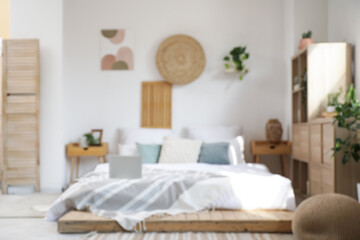 Blurred view of bedroom with laptop on big bed, drawers and plants