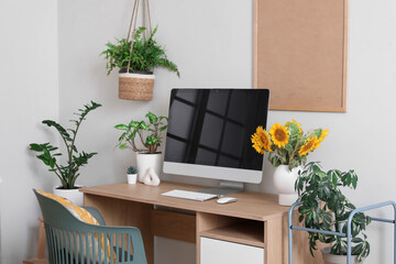 Vase with sunflowers, blank computer monitor and plants on desk in room