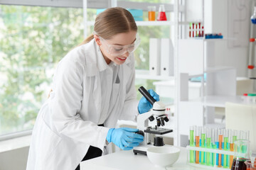 Female chemist with microscope on table in laboratory